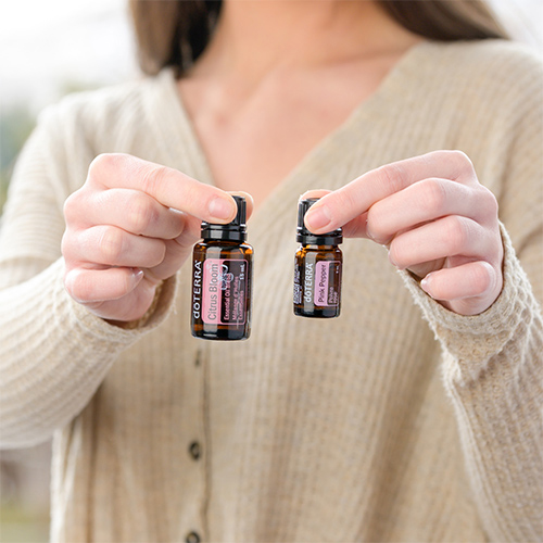 woman holding a pink pepper and a citrus bloom essential oil bottle