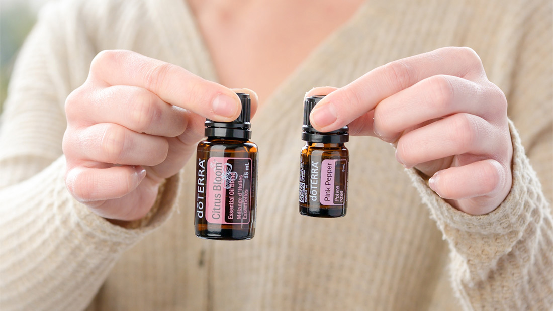 woman holding a pink pepper and a citrus bloom essential oil bottle