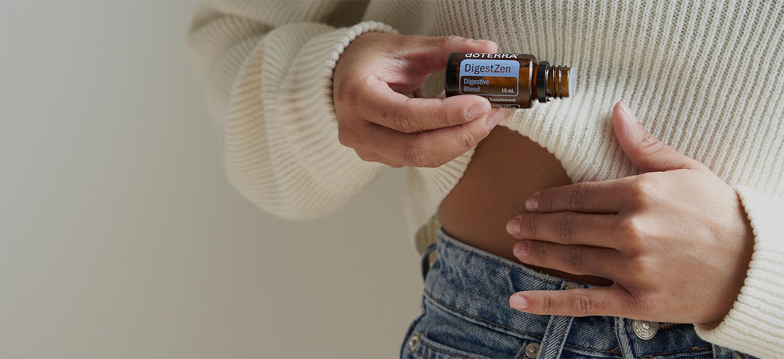 A woman holding DigestZen essential oil and rubbing it on her tummy. 	