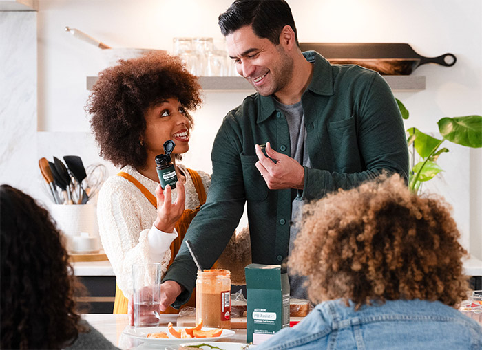 廚房裡一位女士拿著 doTERRA 益生菌膠囊，旁邊有一群人在吃飯