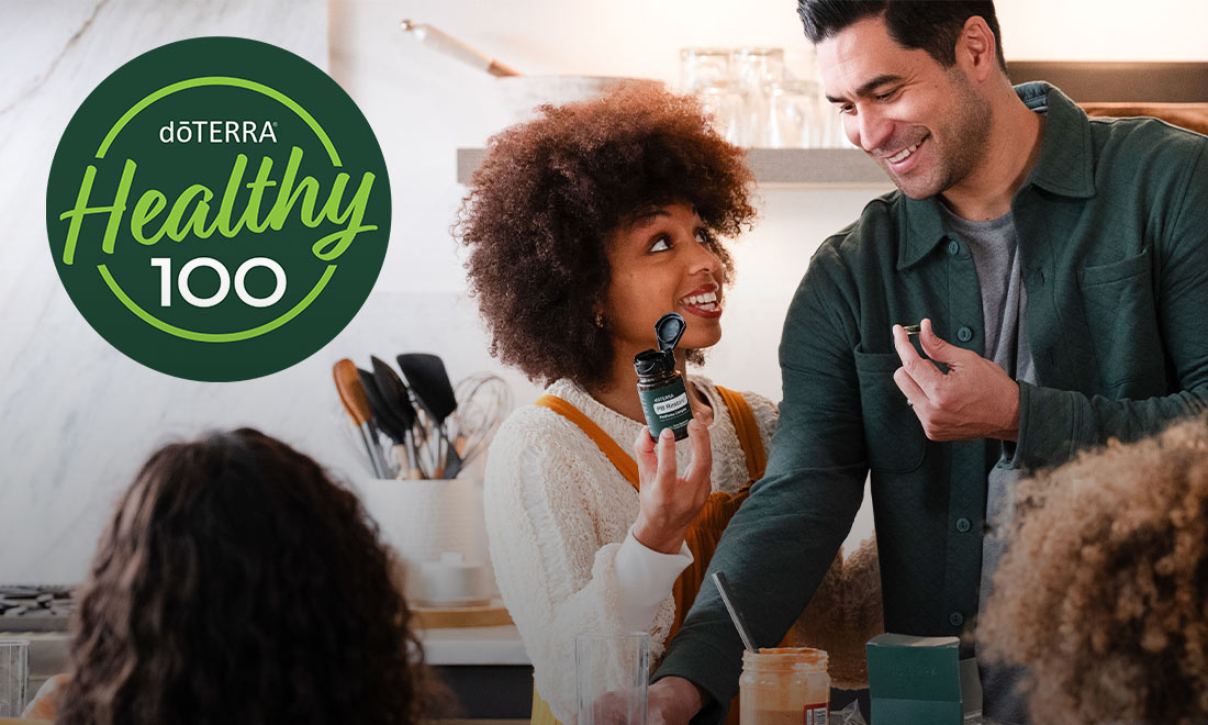 A woman in a kitchen is holding doTERRA PB Restore while a group of people have a meal together.