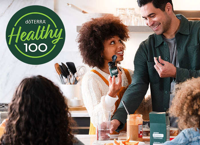 A woman in a kitchen is holding doTERRA PB Restore while a group of people have a meal together.