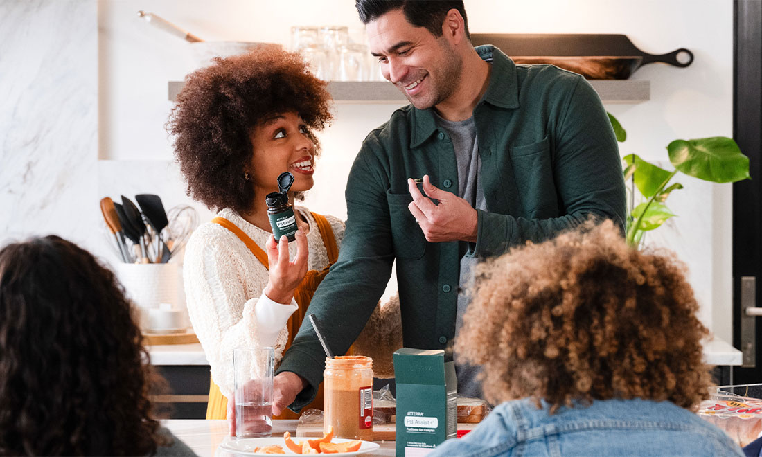 廚房裡一位女士拿著 doTERRA 益生菌膠囊，旁邊有一群人在吃飯