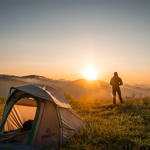 Man out of a tent looking to the sunrise