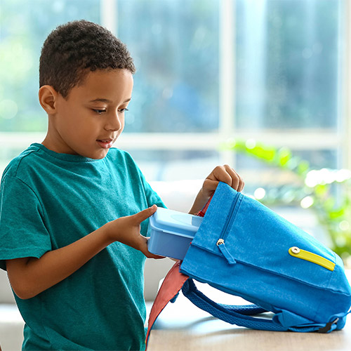 Boy putting lunchbox inside backpack