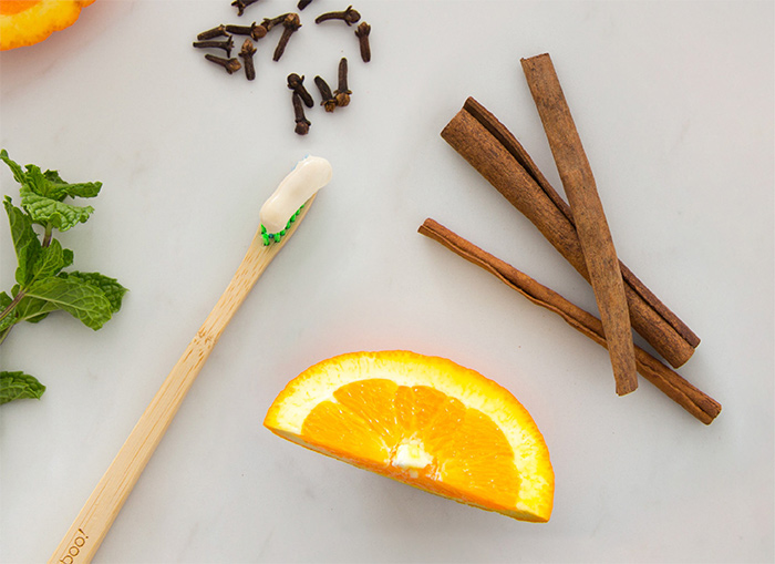 Toothbrush with toothpaste beside mint leaves, orange and cinnamon